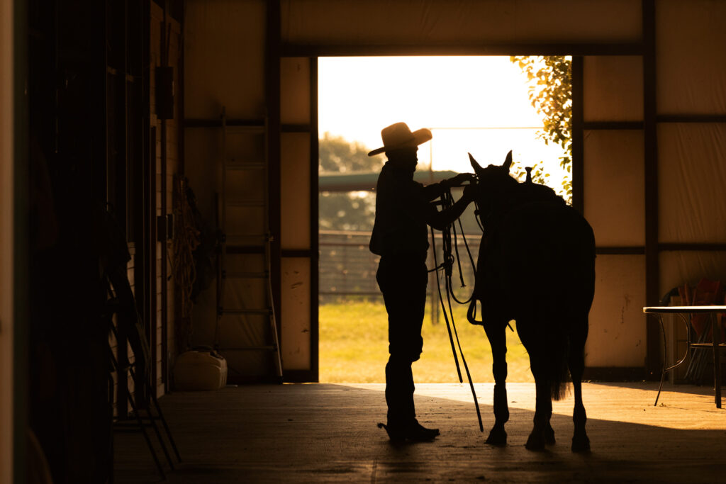 Barn alleyway silhouette tacking up horse cowboy