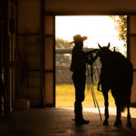 Barn alleyway silhouette tacking up horse cowboy