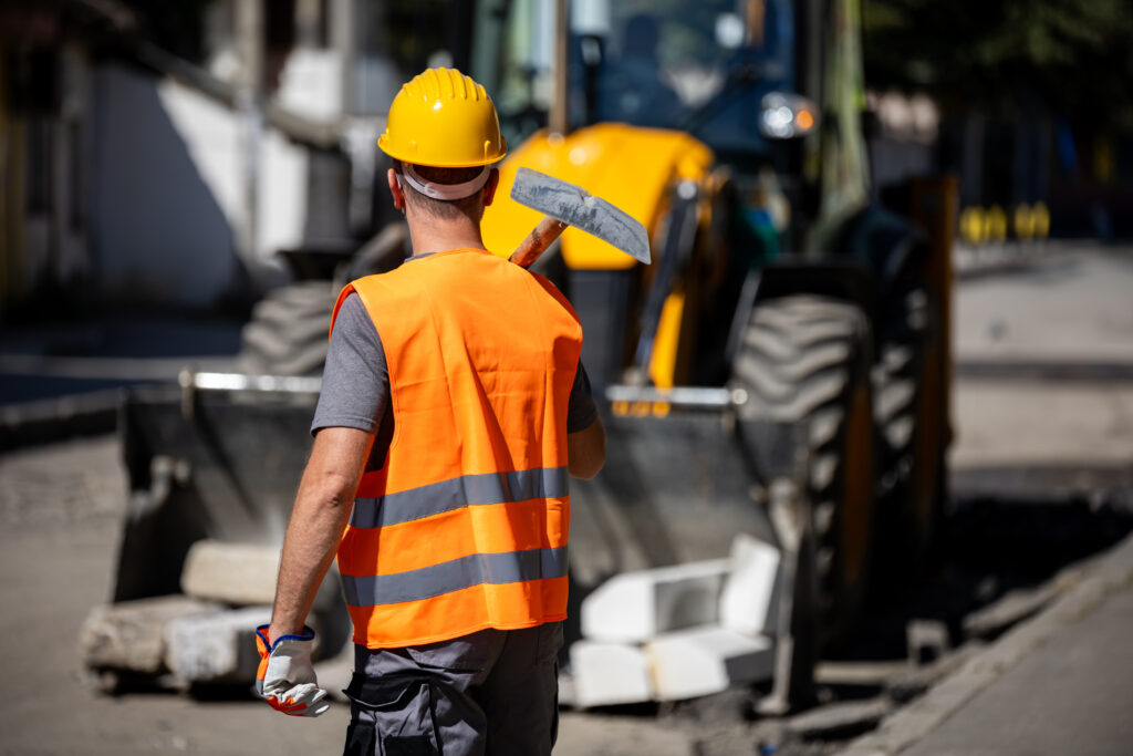 construction worker wearing an orange vest and hard hat stands on a street ready to begin roadwork.