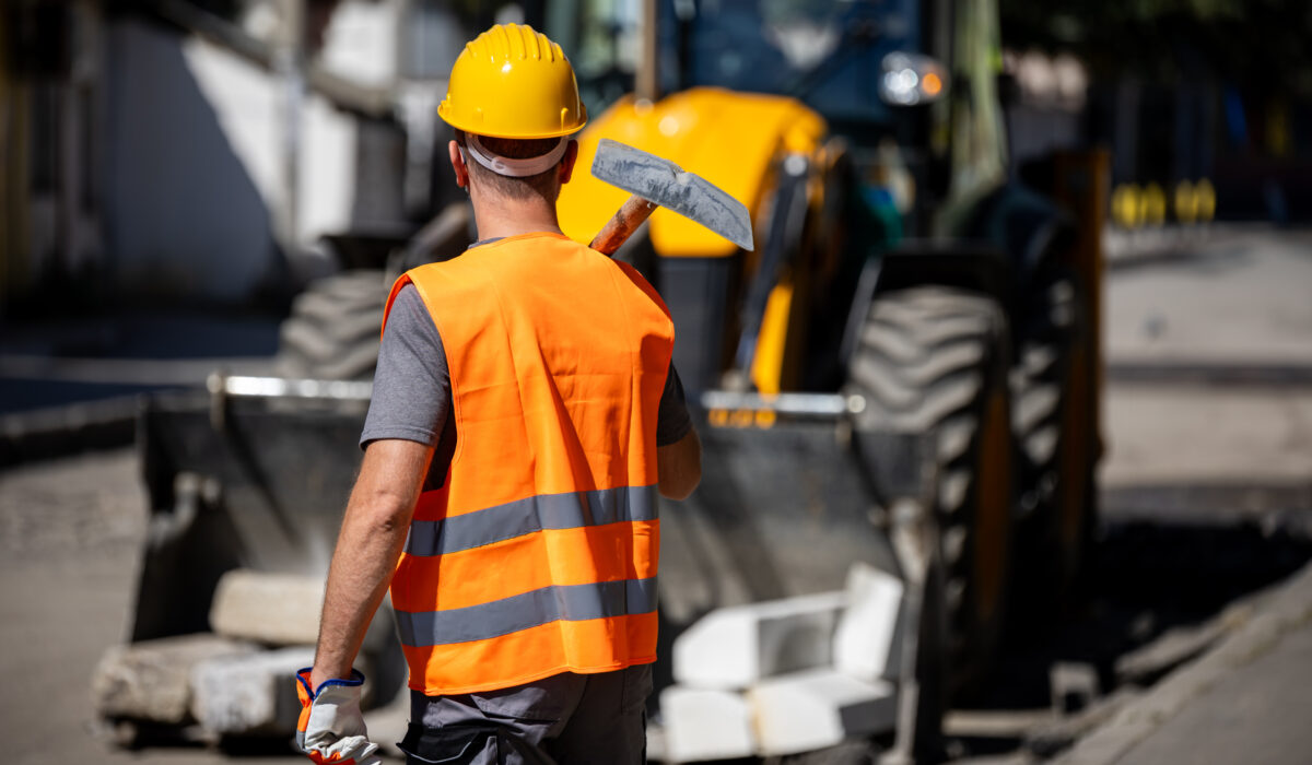 construction worker wearing an orange vest and hard hat stands on a street ready to begin roadwork.