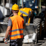 construction worker wearing an orange vest and hard hat stands on a street ready to begin roadwork.