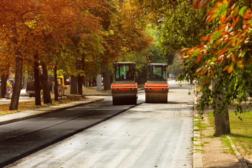 asphalt pavers working on street side by side under autumn trees