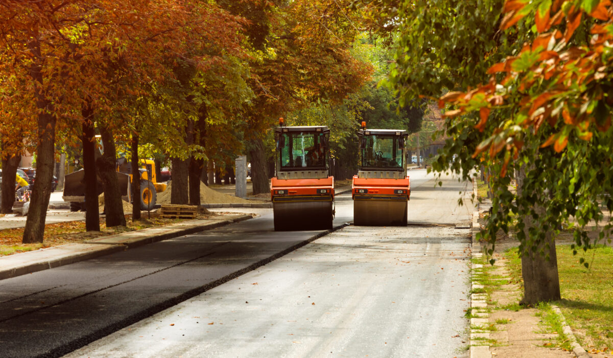 asphalt pavers working on street side by side under autumn trees