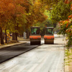 asphalt pavers working on street side by side under autumn trees